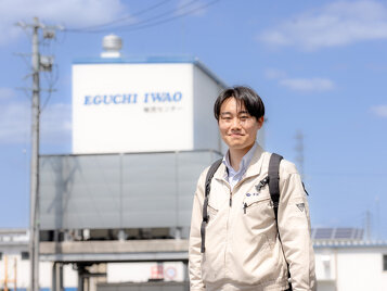 倉庫前に立つ作業着姿のモビリティ第１営業部K.Tさん
