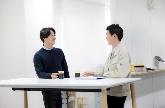 立ちミーティングテーブルで同僚と会話するモビリティ第1営業部O.Rさん